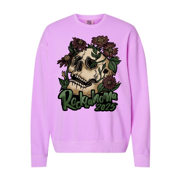 Light pink/lavender crewneck sweatshirt with a large skull graphic surrounded by blooming purple flowers and green leaves. Text reads “Rocklahoma 2025” in dark green lettering.